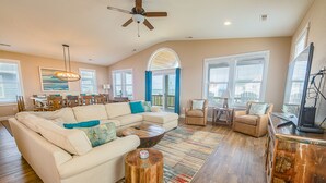 A spacious living room with a sectional sofa, a coffee table, and a TV. There is a dining area with a table and chairs, and a balcony with a view. - Steps to the Sand-Ocean Views-Hot Tub/Heated Pool-Putting Green-Coffee Bar (Kitty Hawk)