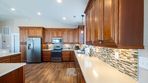 A modern kitchen with wooden cabinets, stainless steel appliances, and a tiled backsplash. - Steps to the Sand-Ocean Views-Hot Tub/Heated Pool-Putting Green-Coffee Bar (Kitty Hawk)