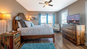 A bedroom with a bed, a dresser, a television, a ceiling fan, and a window with curtains. - Steps to the Sand-Ocean Views-Hot Tub/Heated Pool-Putting Green-Coffee Bar (Kitty Hawk)