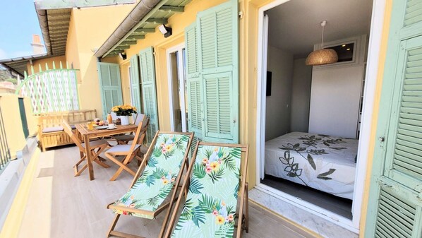 Ein Balkon mit Holzmöbeln, einem Tisch mit Blumenvase und einem Bett mit floralem Überwurf.