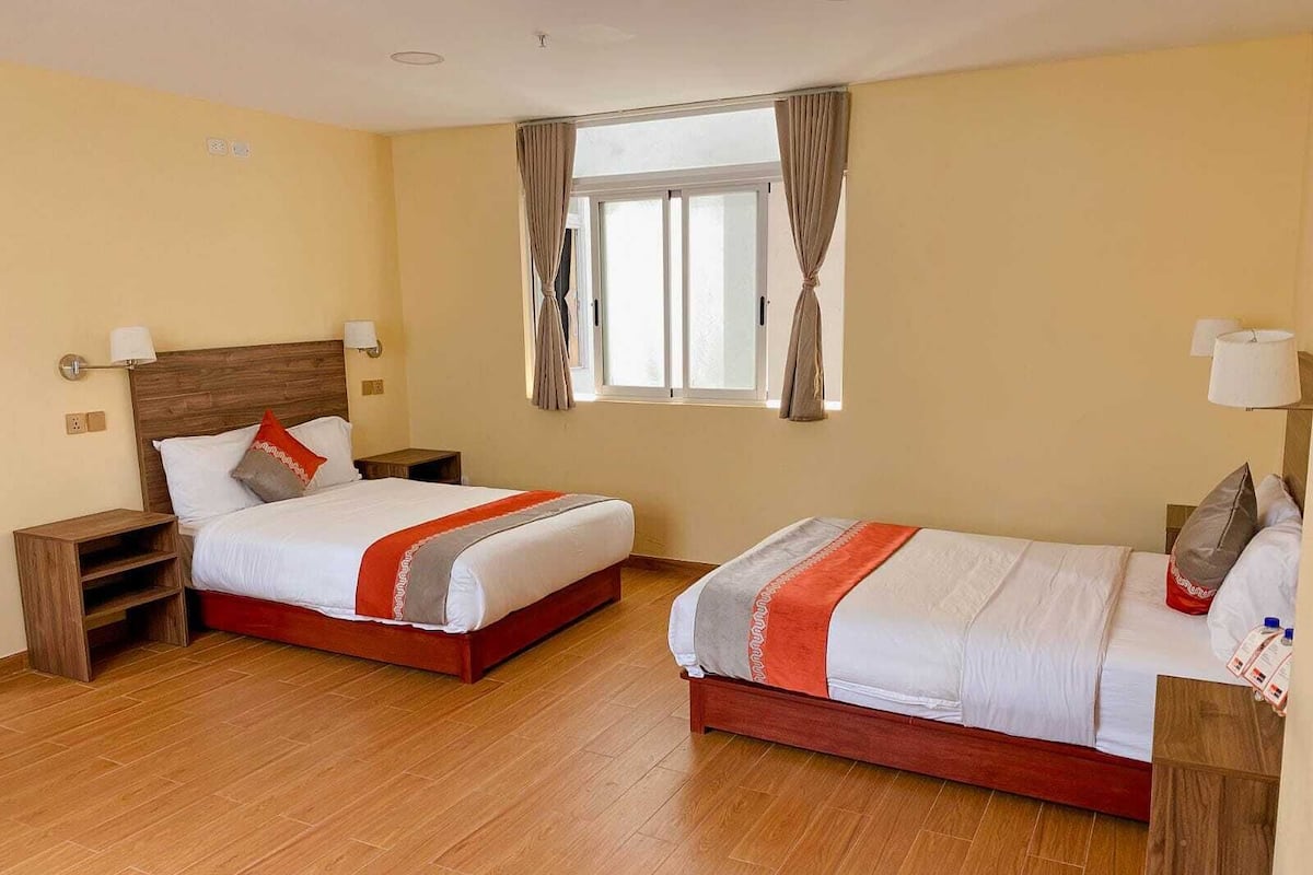 Habitación de hotel con dos camas, piso de madera y ventana con cortinas.