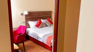 Une chambre d’hôtel avec un lit en bois, des oreillers rouges et blancs, une chaise rouge et une table de chevet.