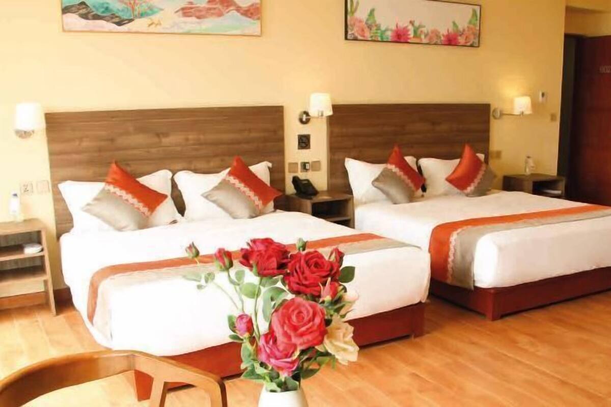 Habitación de hotel con dos camas, cabeceros de madera, ropa de cama blanca y un florero con rosas rojas.