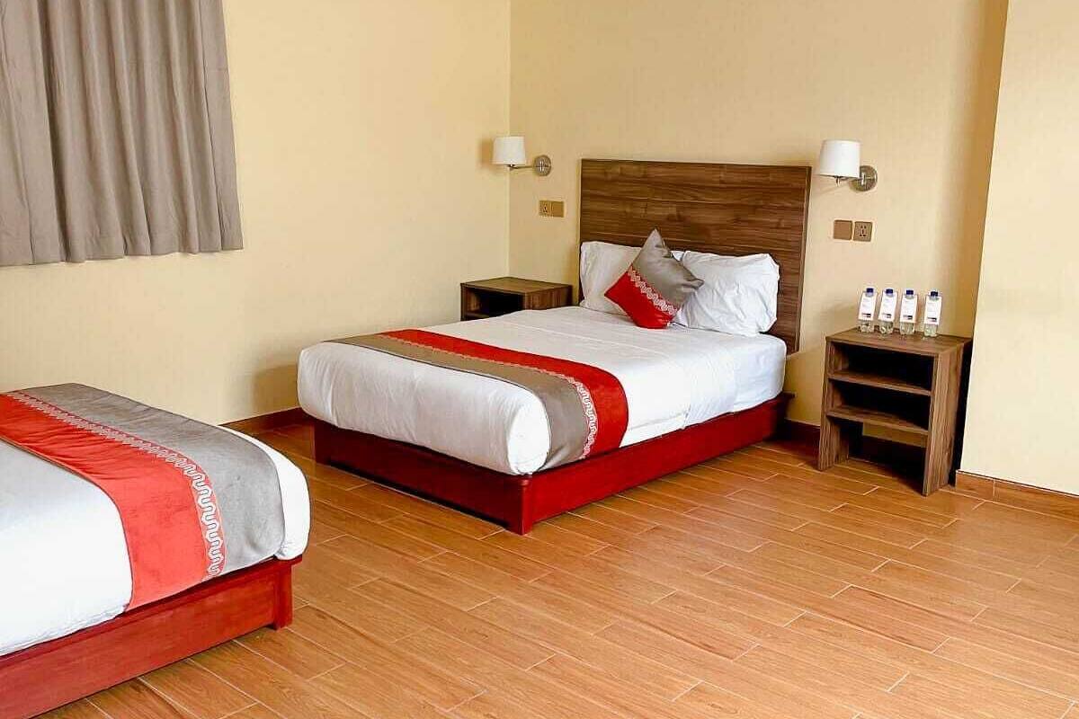 Habitación de hotel con dos camas, suelo de madera y una paleta de colores neutros.