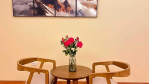 En matplats med ett runt träbord, två stolar och en vas med röda blommor. Ovanför bordet hänger en stor, inramad tavla som föreställer ett berglandskap.