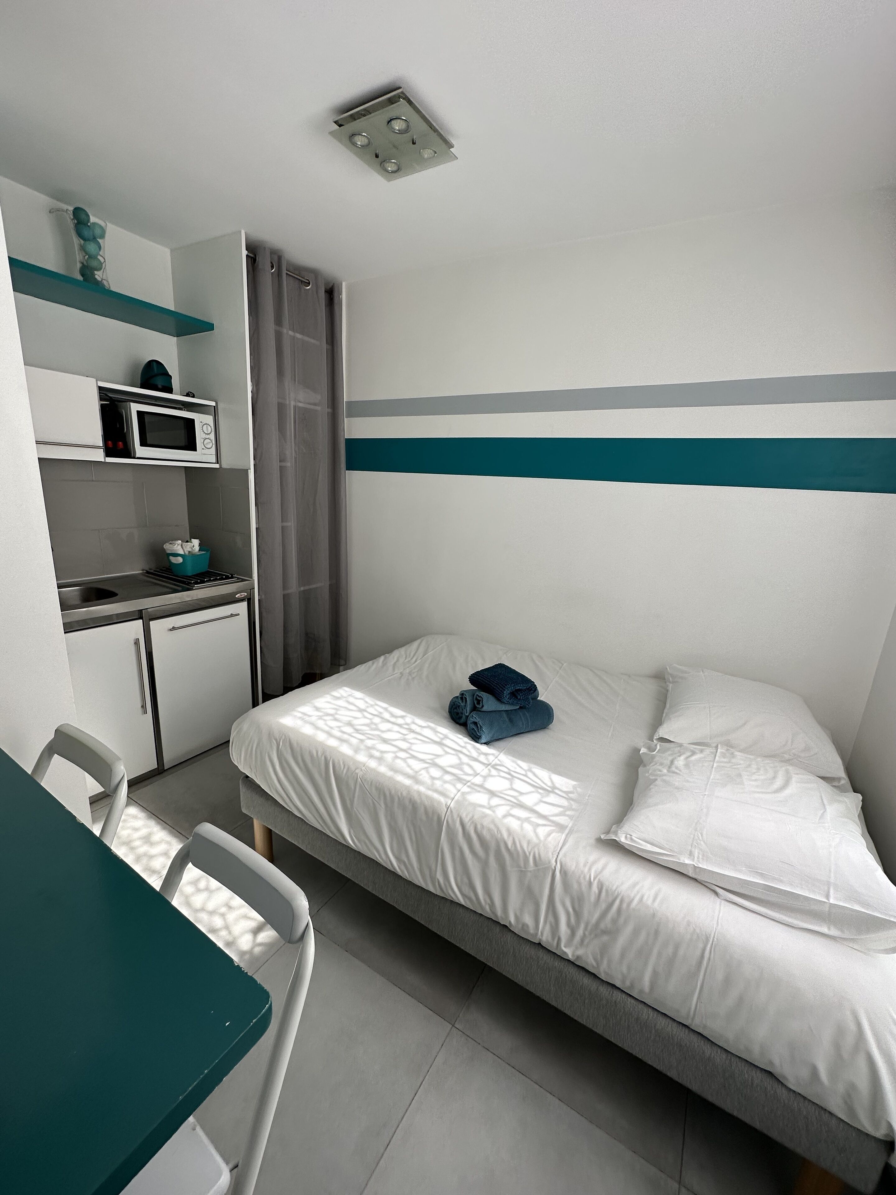 A compact hotel room with a bed, a desk, a microwave, and a shower.