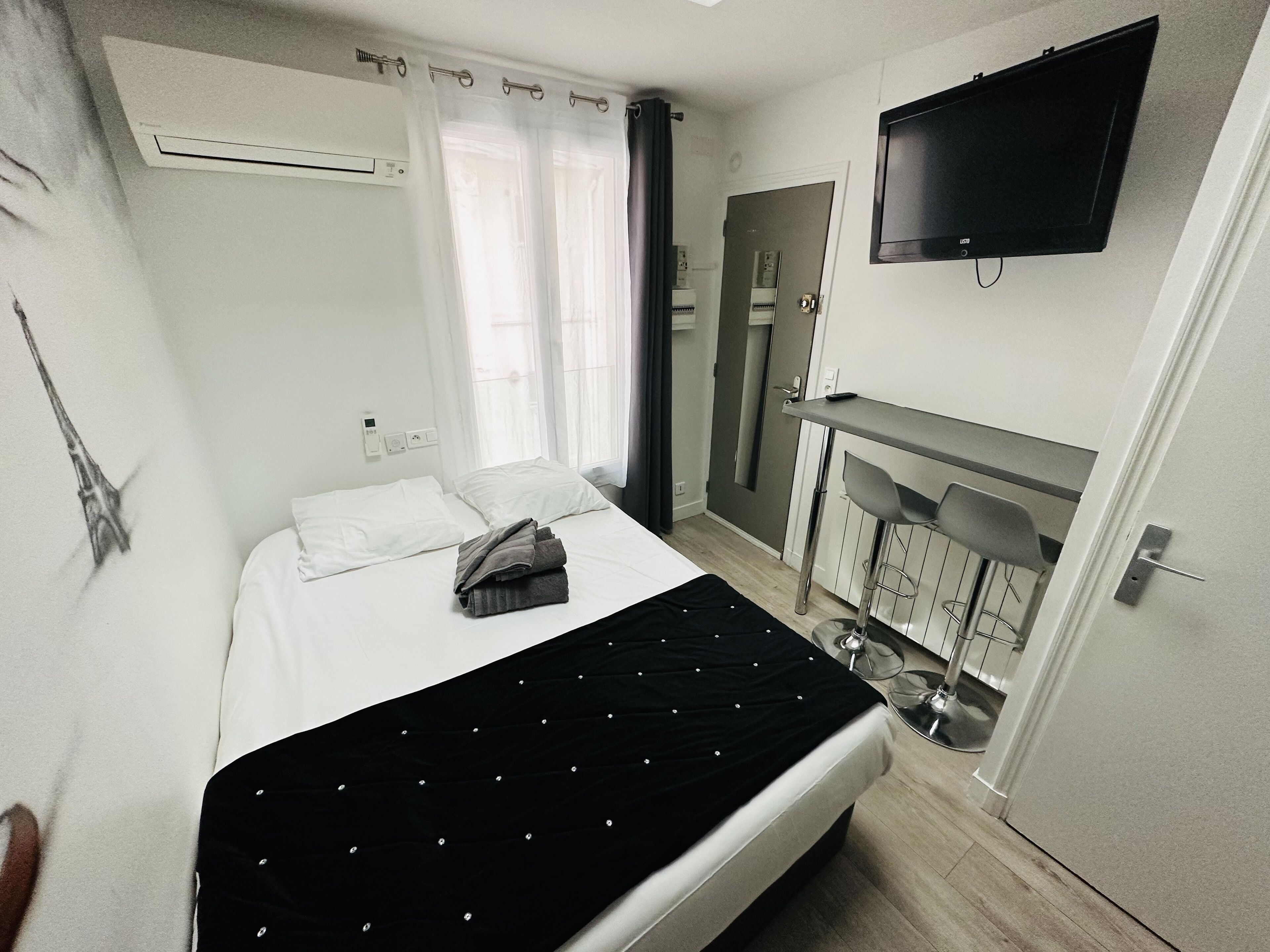 A hotel room with a bed, a TV mounted on the wall, a bathroom with a mirror, and a door leading to another room.