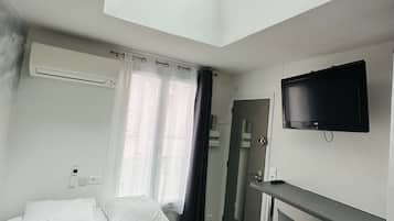 Una habitación de hotel moderna con tragaluz, cama con ropa de cama blanca, manta negra, televisor de pantalla plana y un pequeño bar.