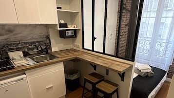A compact kitchen with a built-in stove, white cabinets, and a wooden countertop. There is a small stool and a bench with towels.