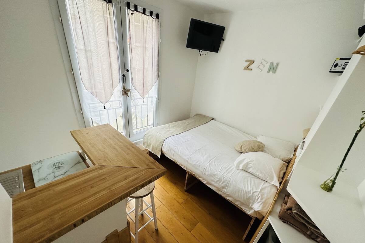 A small, neatly arranged bedroom with a single bed, a wooden desk, and a TV mounted on the wall.