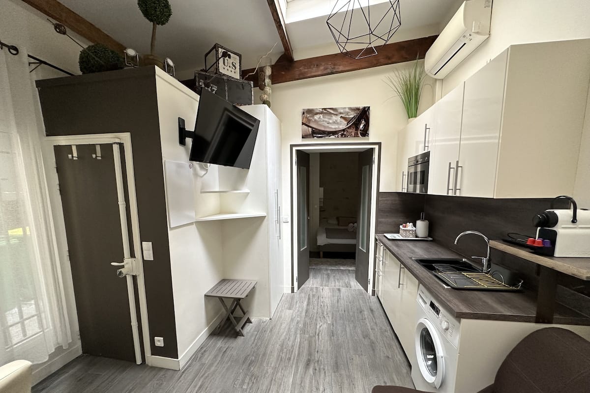A compact kitchen with a washing machine, a small dining area, and a TV mounted on the wall.