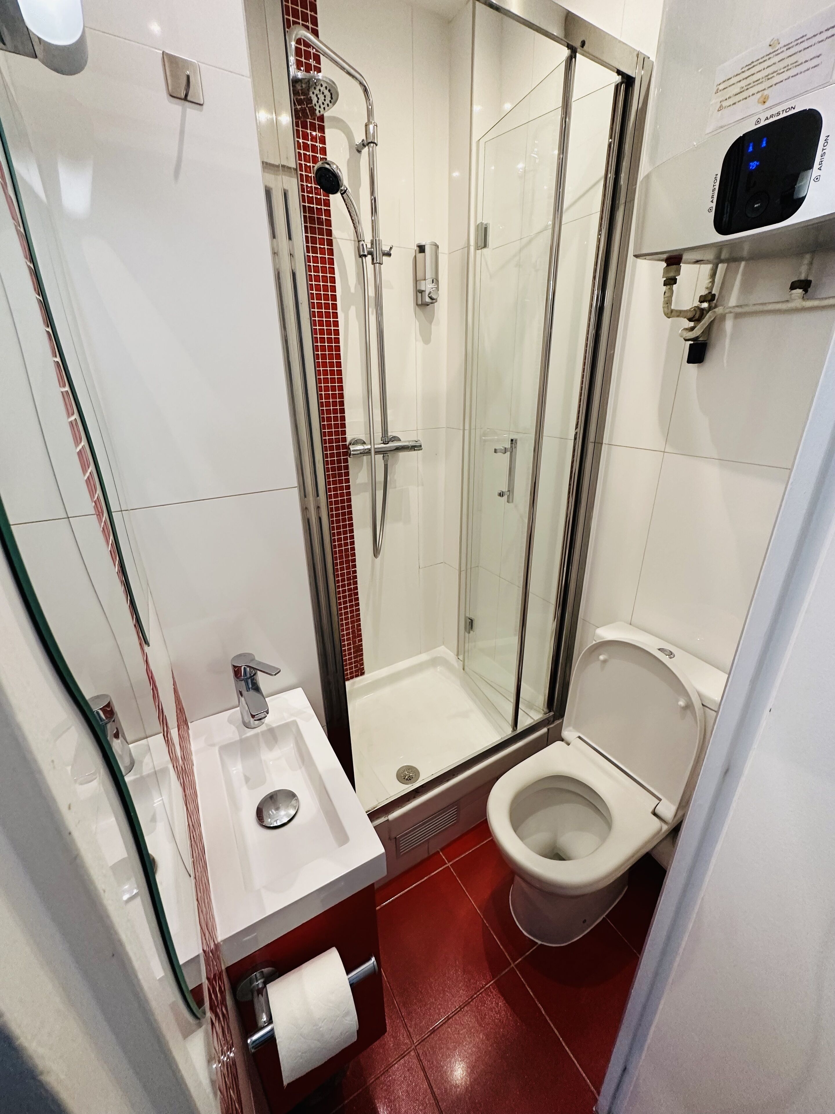 A modern bathroom with a glass-enclosed shower, a toilet, and a sink with a paper towel dispenser.