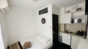 A compact room with a bed, a small kitchenette, a wall-mounted TV, and a door leading to another room.