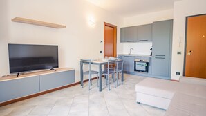 A compact living space with a TV, dining table, chairs, kitchenette, and a sofa. - Residence San Francesco (Desenzano del Garda)