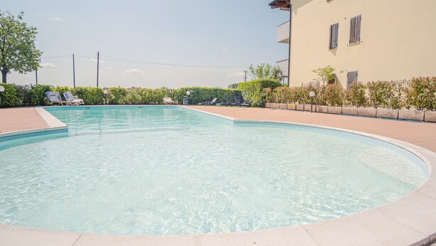A clear swimming pool with lounge chairs and a building in the background. - Residence San Francesco (Desenzano del Garda)