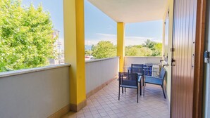 A balcony with yellow pillars, a tiled floor, and a view of trees and buildings. - Residence San Francesco (Desenzano del Garda)