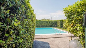 Piscina retangular rodeada por sebes bem aparadas.