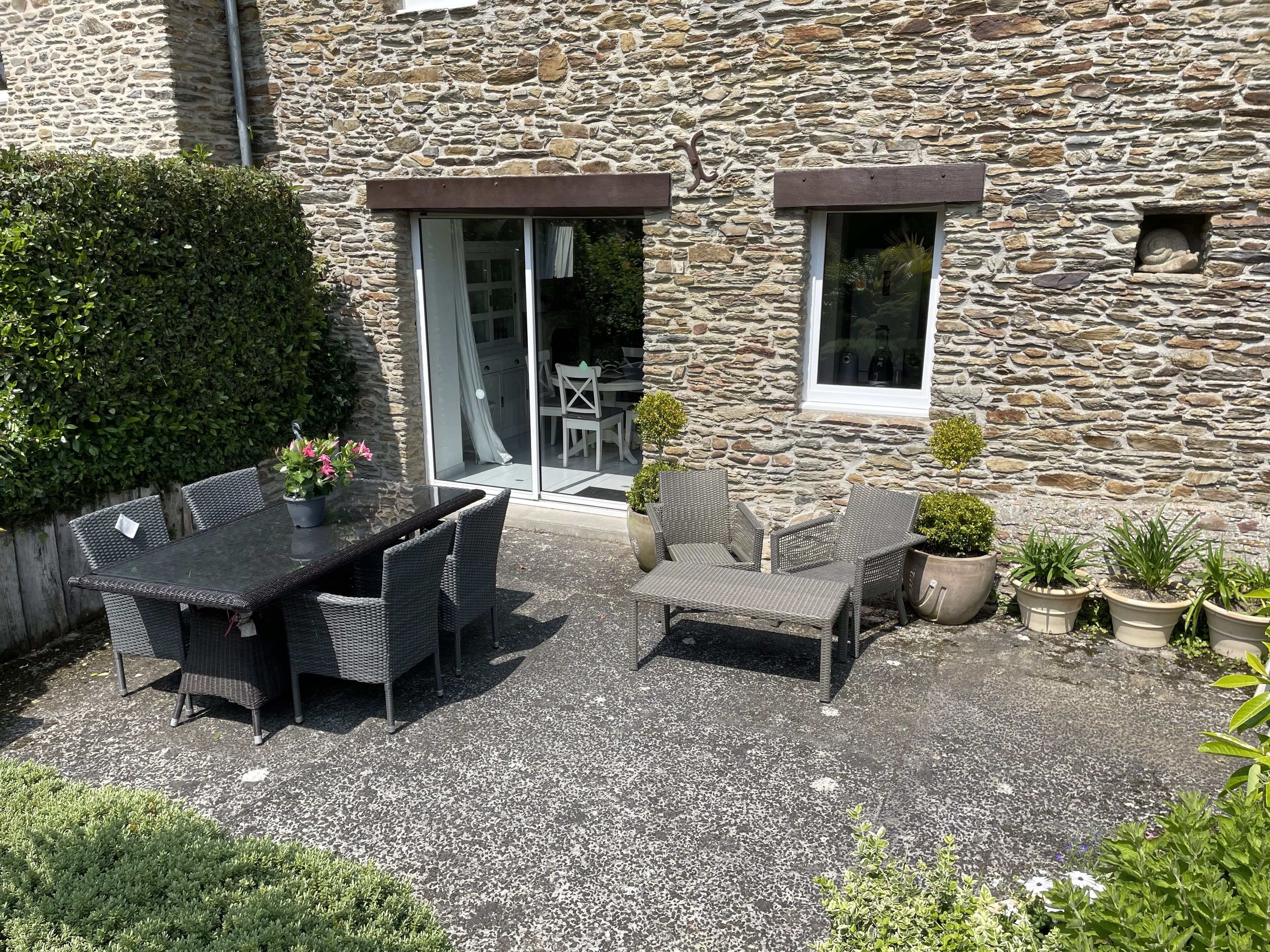 An outdoor patio area with a stone wall, a dining table with chairs, and potted plants.