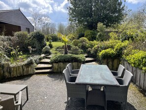 A garden patio with wicker furniture, a stone pathway, and a variety of plants and trees. - Le Courtil 3* (Cerisy-la-Forêt)