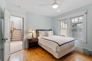Ein Schlafzimmer mit Bett, Nachttisch, Lampe und Blick ins Freie durch ein Fenster.