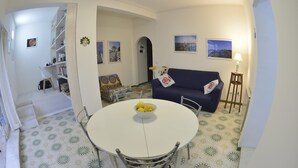 A dining area with a round table and chairs, a blue sofa, and a small side table with a lamp. - An apartment nestled in the sun 110 meters from the sea (Scauri)