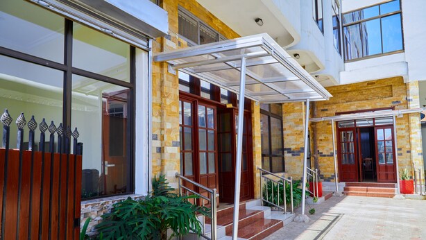 Edifici amb entrada coberta, escales cap a la porta i plantes en testos a prop de la façana.