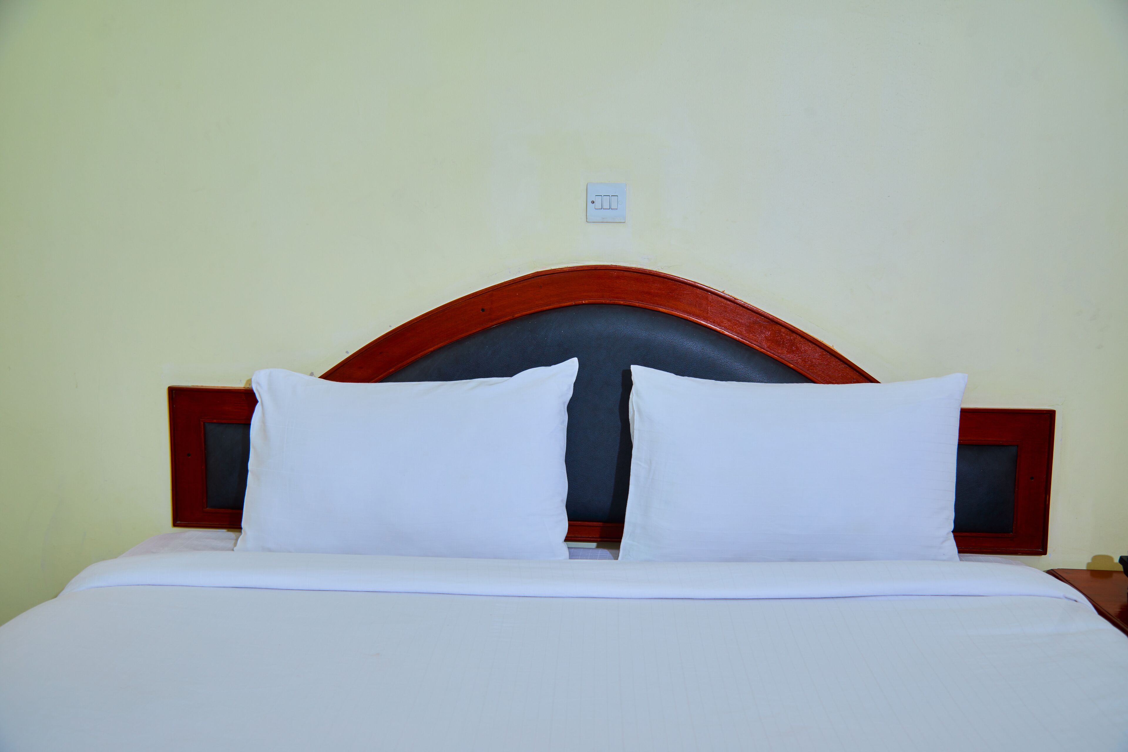 Una cama con cabecera de madera, ropa de cama blanca y un interruptor de luz pequeño en la pared.