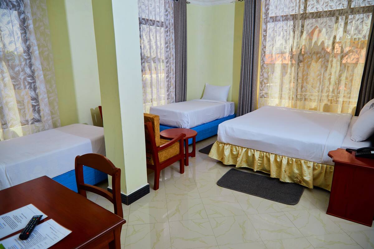 A hotel room with two single beds, a wooden chair, a small table with a remote control, and a desk with papers.