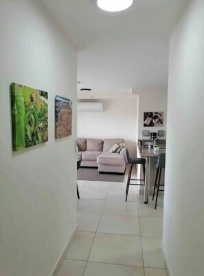 A narrow hallway leading to a living area with a sofa and a dining area with a table and chairs.