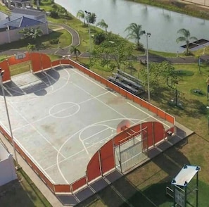 An outdoor basketball court with a red and grey color scheme, surrounded by greenery and a body of water. - Ocean View Apartment (Vacamonte)