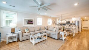 Ein geräumiges Wohnzimmer mit Ecksofa, Couchtisch und Essbereich. Im Hintergrund ist eine Küche zu sehen.