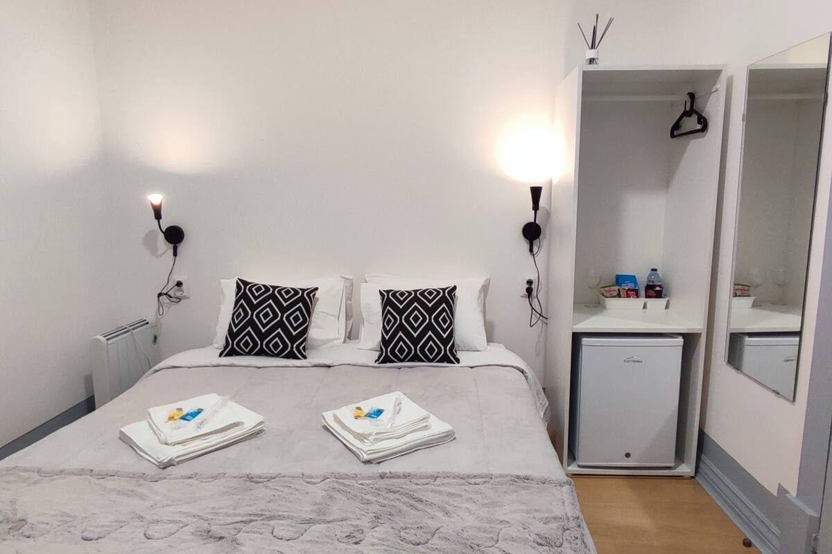 Een keurig opgemaakt hotelkamer met een bed, twee bedlampen, een klein nachtkastje met toiletartikelen en een spiegel.