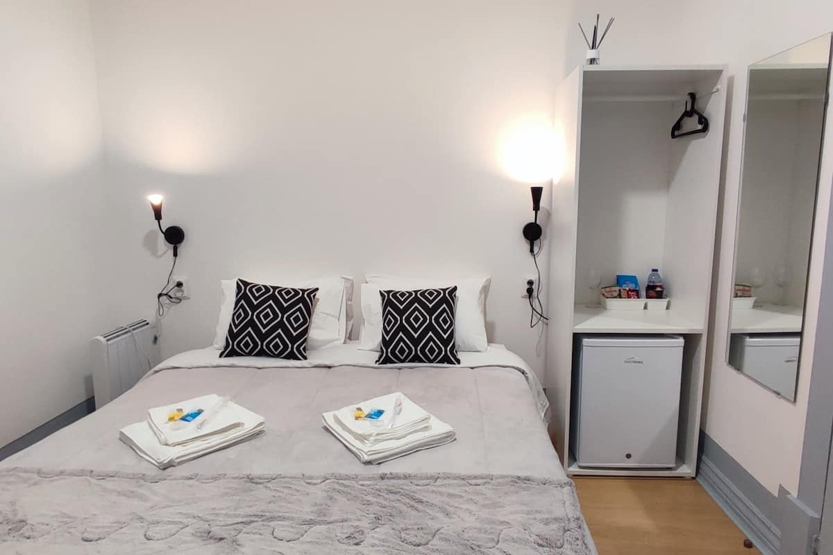 Hotellihuone, jossa on sänky, kaksi yöpöytälamppua, pieni valkoinen kaappi, peili ja ovi.