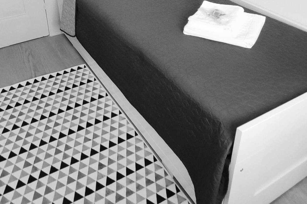 Een zwart-wit kamer met een bed, een kamerbreed tapijt met een patroon en een ingelijst beeld aan de muur.