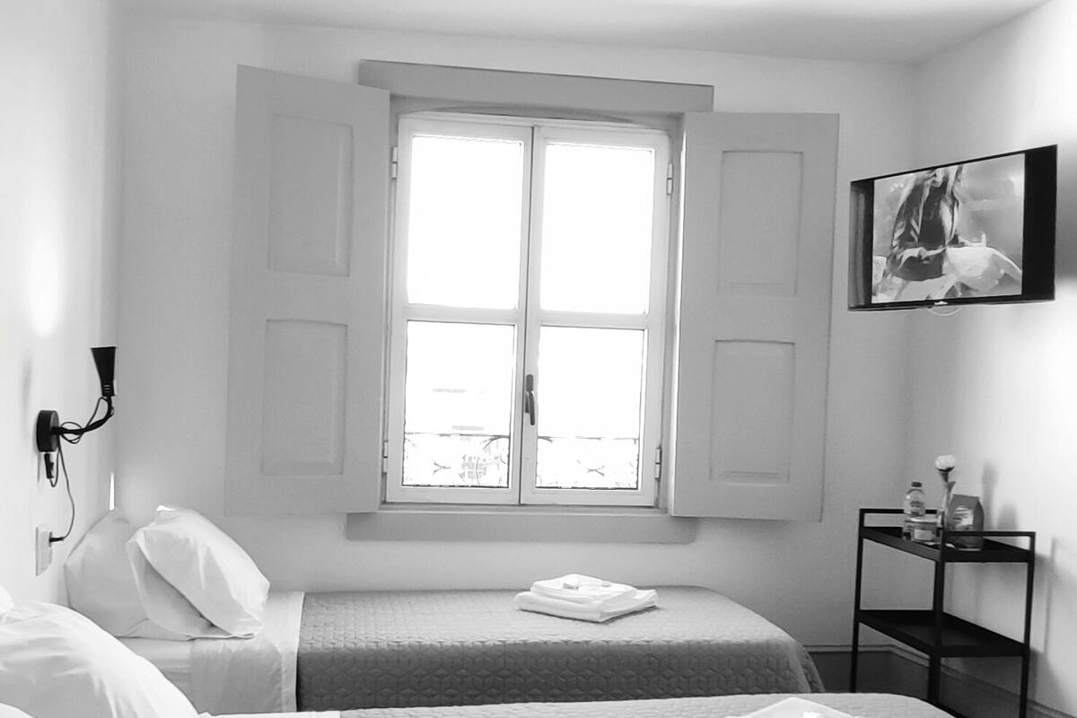Hotelkamer met twee bedden, een raam, een televisie en een klein tafeltje met toiletartikelen.