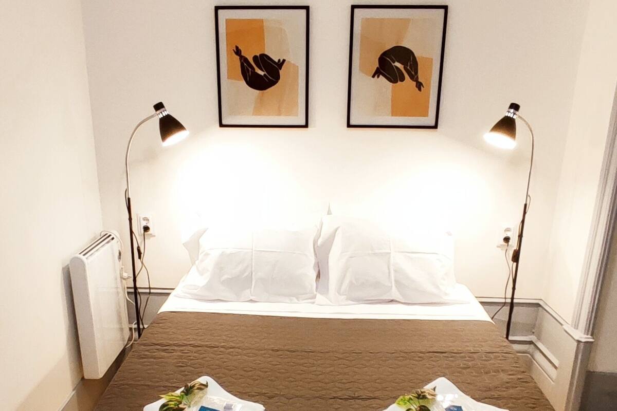 Een hotelkamer met een bed, twee bedlampen en twee kunstwerken in lijsten aan de muur.