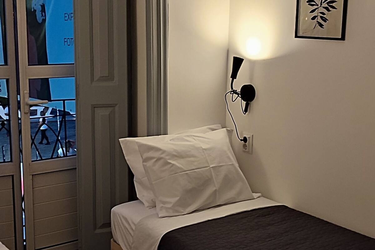Een hotelkamer met twee bedden, een groot raam met uitzicht op een gebouw en een wandlamp.