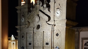 Ein historisches Gebäude mit aufwendigen architektonischen Details und einem Uhrturm, aufgenommen aus der Perspektive der Straßenansicht bei Nacht.