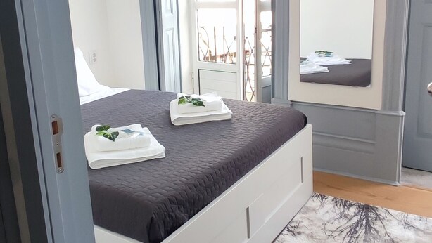 A modern bedroom with a bed, a large window, and a flat-screen TV. - Vila Santa Cruz Guest House (Braga)