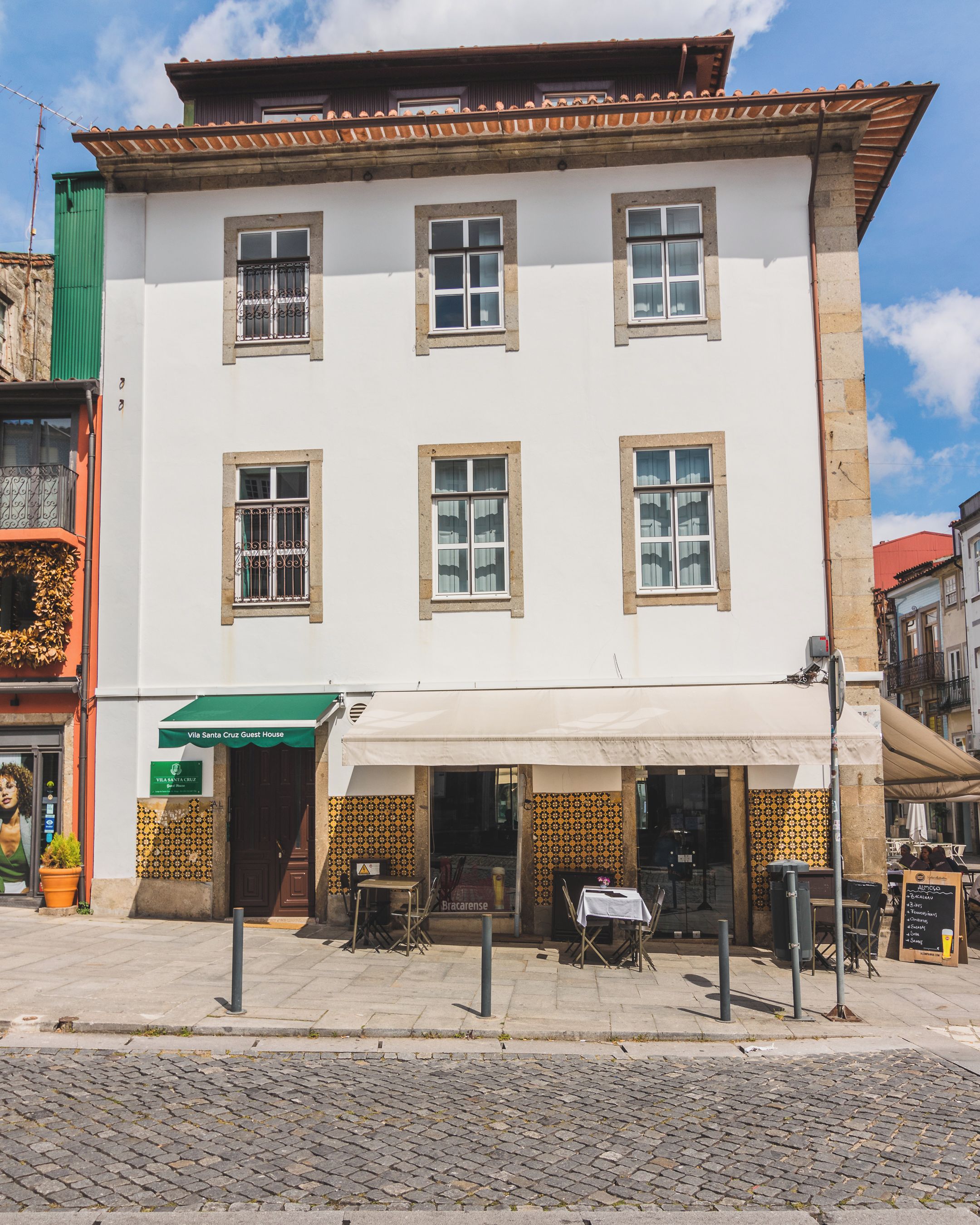 Ein zweistöckiges Gebäude mit weißer Fassade, zahlreichen Fenstern und einem überdachten Außenbereich zum Sitzen.