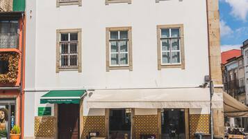 Ein zweistöckiges Gebäude mit weißer Fassade, zahlreichen Fenstern und einem überdachten Außenbereich zum Sitzen.