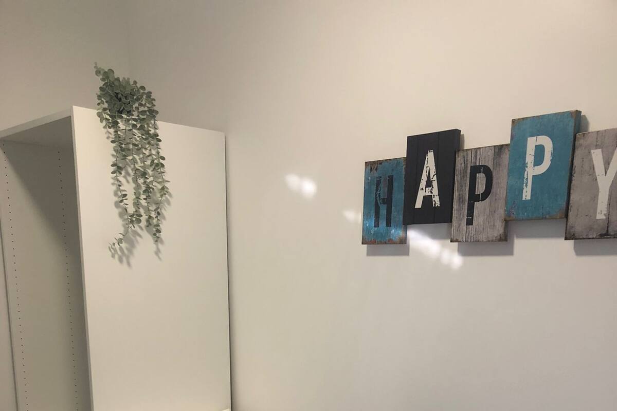 Een slaapkamer met een bed, kussens, een hangplant en een bordje met de tekst 'HAPPY'.
