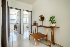 Un interior moderno con un banco de madera, un espejo decorativo y una planta en maceta sobre una consola.