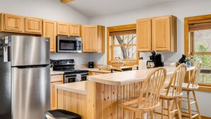 A modern kitchen with wooden cabinets, stainless steel appliances, and a bar area with wooden stools.