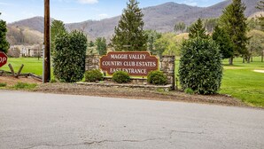 A sign for Maggie Valley Country Club Estates East Entrance with a view of a golf course and mountains in the background.