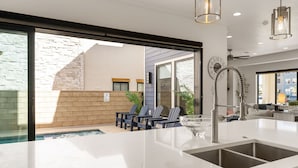 Une cuisine moderne dotée d’un grand îlot central, d’un évier intégré et donnant sur la terrasse extérieure.