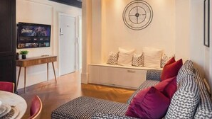 A modern living room with a sofa, a television, a clock, and a bench with cushions.