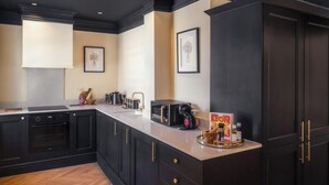 A kitchen with dark cabinetry, a countertop, a coffee maker, and framed artwork on the wall.