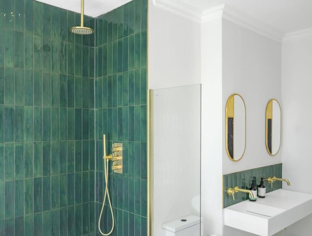 Un baño con ducha, dos espejos, lavamanos e inodoro.