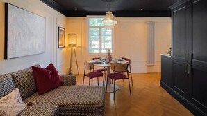 A living room with a sofa, a dining table with chairs, a chandelier, and a large window.